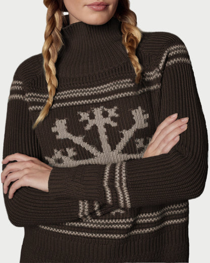 Woman wearing a brown knit sweater with a pattern and matching beanie with 'APRES' text against a textured gray background.