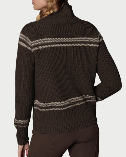 Person wearing a brown sweater with white patterns and matching brown beanie against a gray background