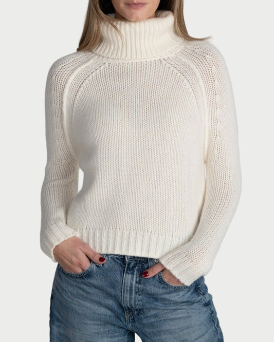 Woman wearing a white turtleneck sweater and blue jeans against a plain background