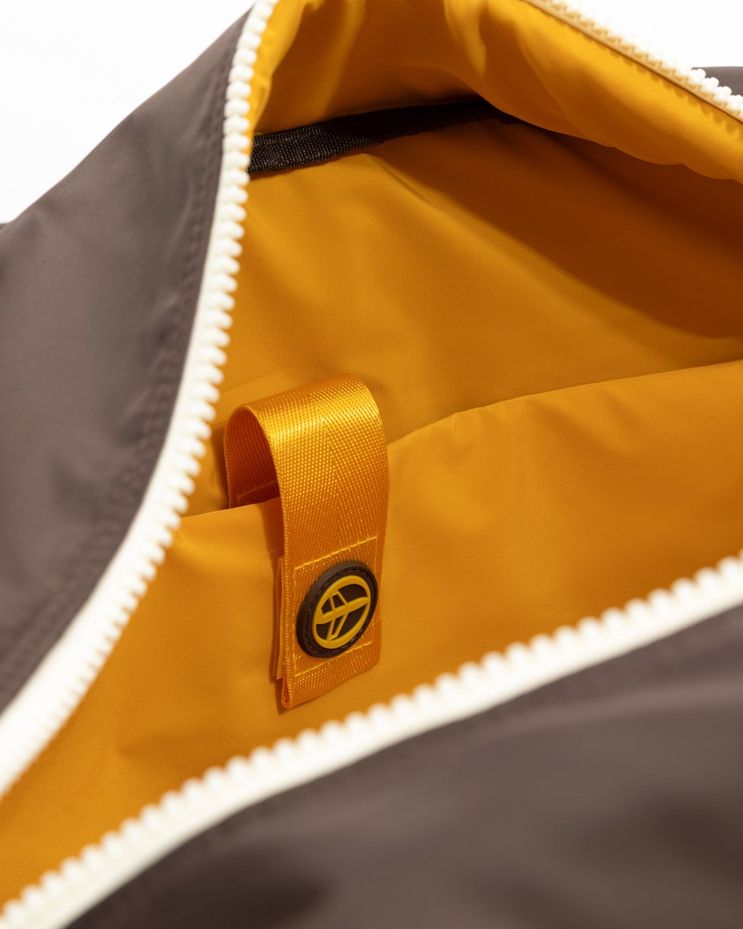 A close-up of the Oncept Olympia Travel Bag by Oncept shows its open white zipper, a bright yellow-orange interior, fabric loop, and a circular black and yellow logo tag inside.