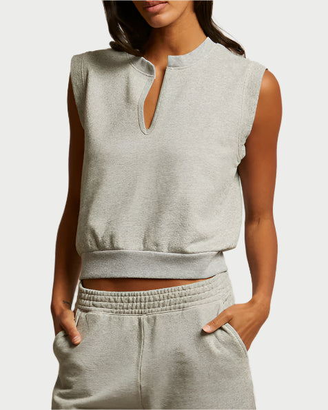 A woman wears a light gray Sloane Terry Split Top by perfectwhitetee with matching high-waisted sweatpants. Made from soft french terry, her hands are in her pockets and her face is partially out of frame.
