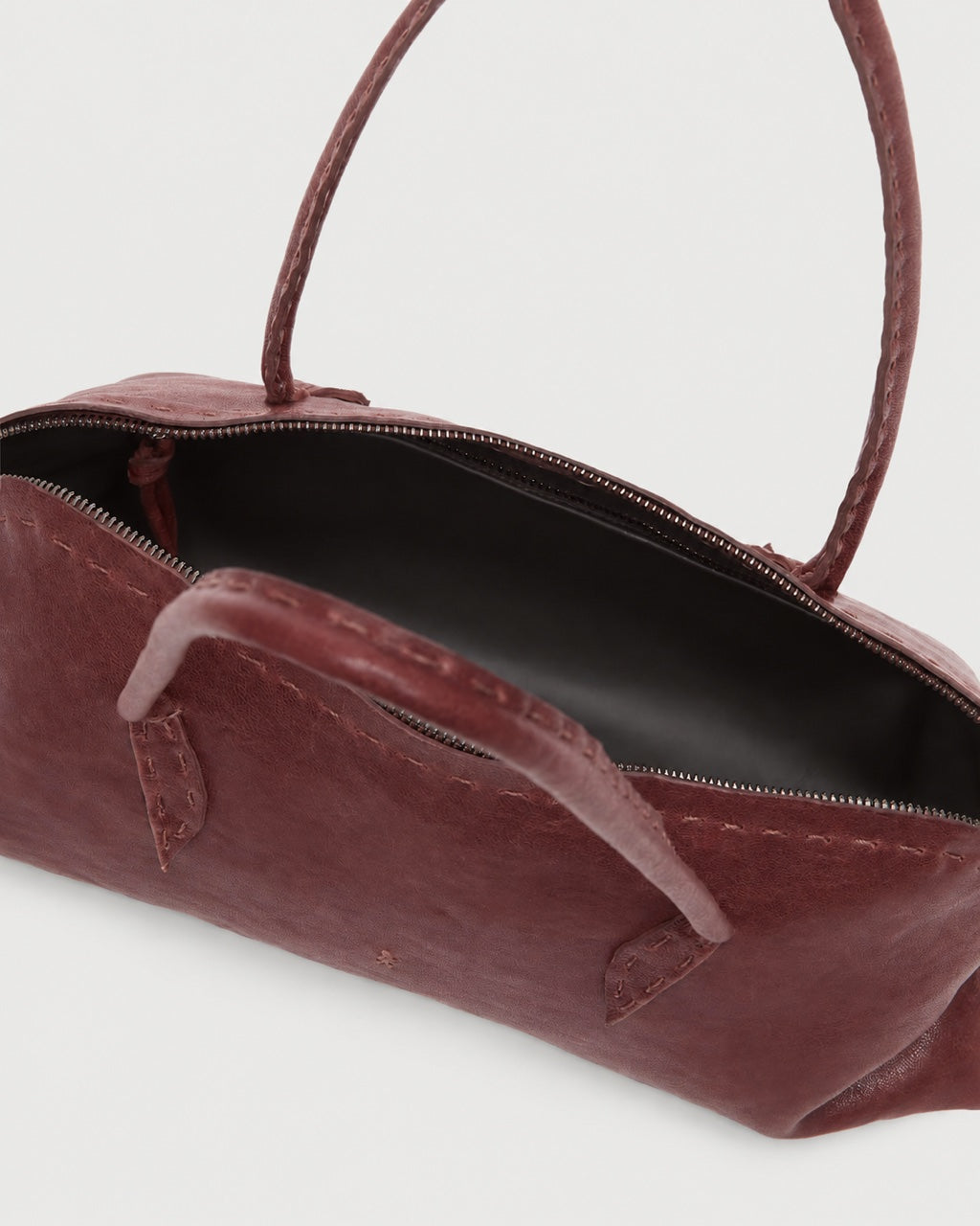 A dark red leather Henry Beguelin Bolla Bassa Bag with a top handle and a zipper closure, showcasing fine Italian craftsmanship.