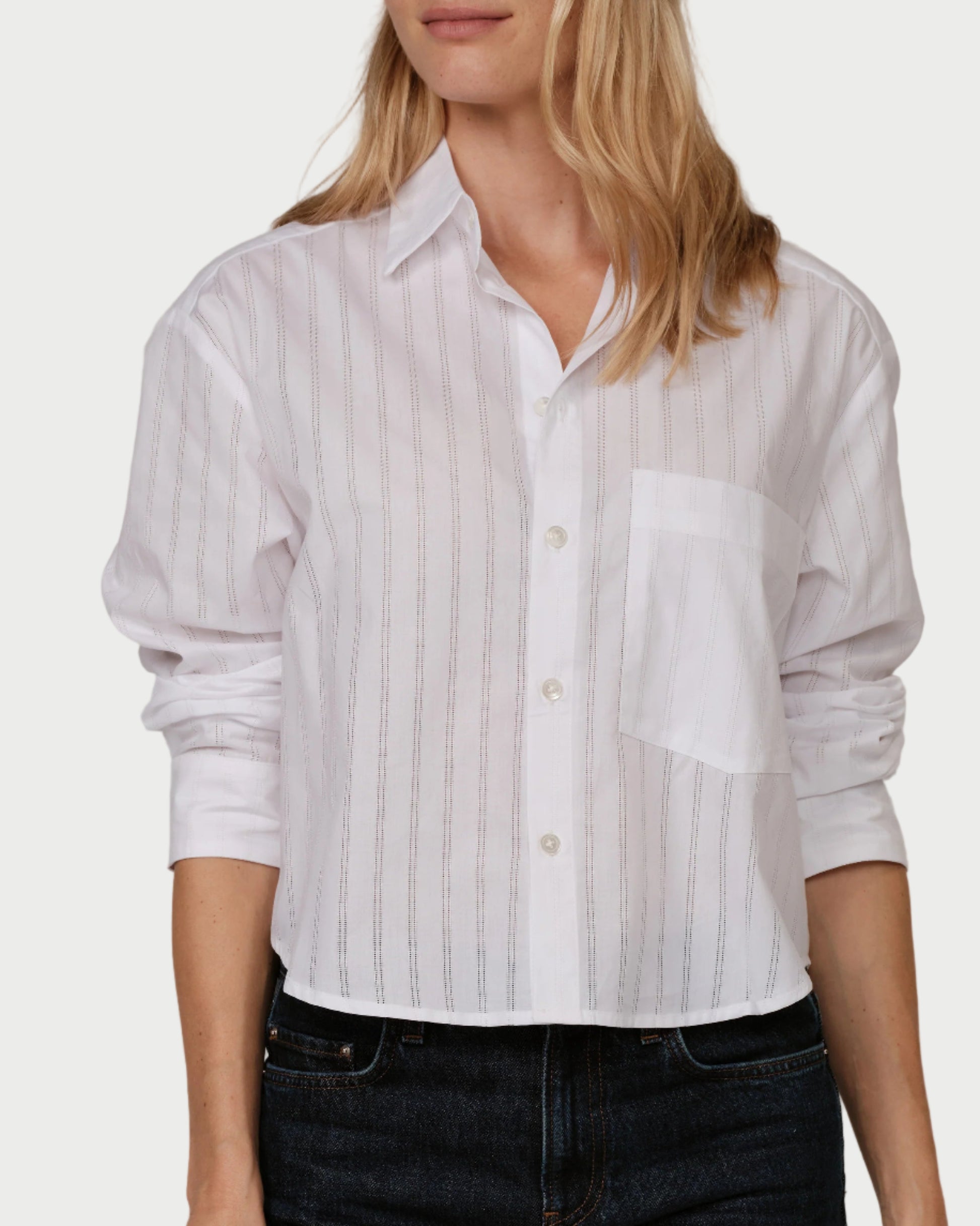 Woman wearing a white striped shirt and dark jeans against a plain background