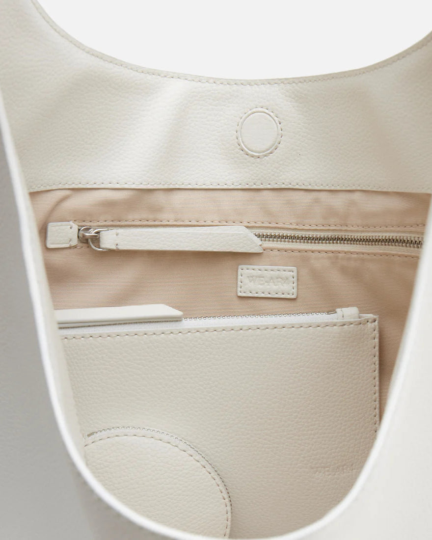 Close-up view of the inside of The H Hobo Bag by WE-AR4, made from upcycled grain leather, featuring a zippered pocket, an open pocket, and a white object—potentially a phone or notebook—in a slip pocket.