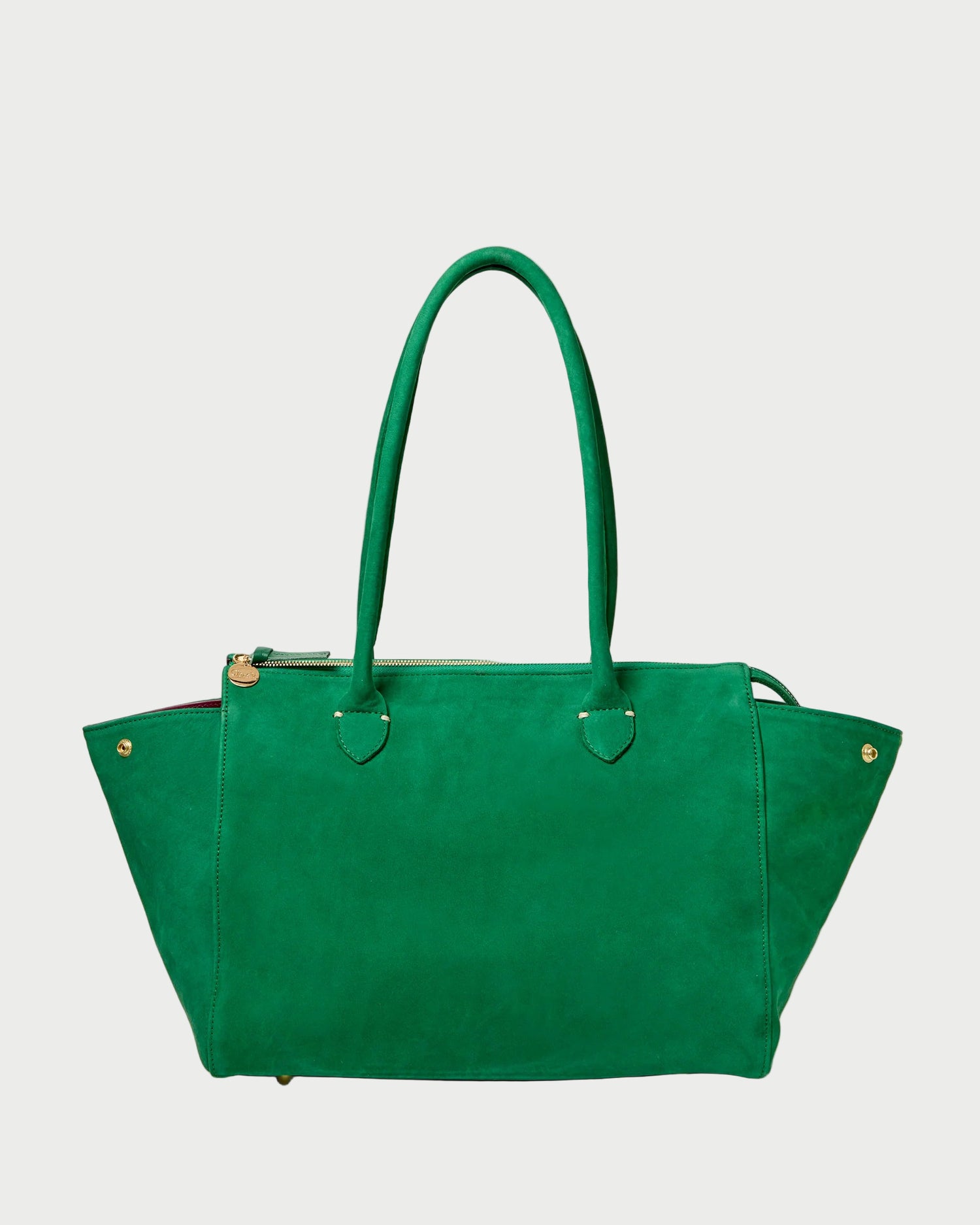 The CLARE V. Beatrice Tote Bag is a large, structured emerald green suede tote with double handles, gold-tone accents, and a top zipper, shown against a white background.