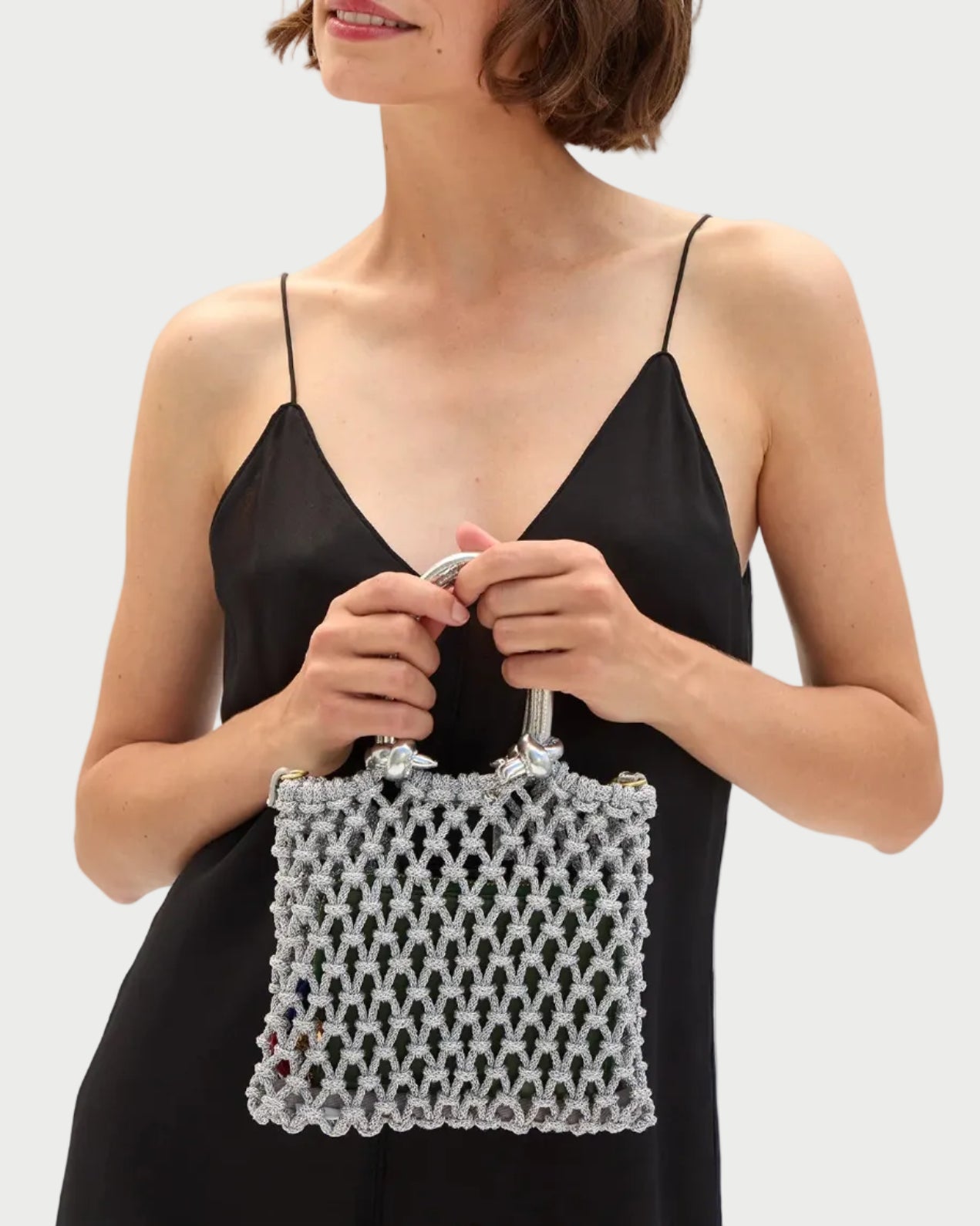 Woman holding a white beaded handbag against a plain background