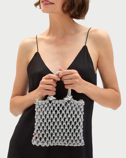 Woman holding a white beaded handbag against a plain background