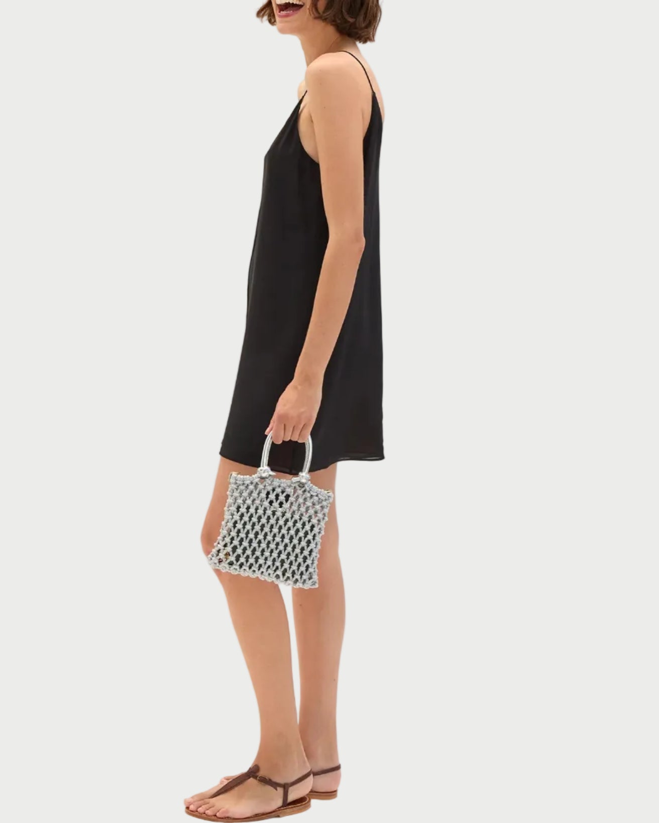 Woman in a black dress holding a patterned handbag on a white background