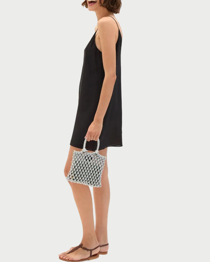 Woman in a black dress holding a patterned handbag on a white background