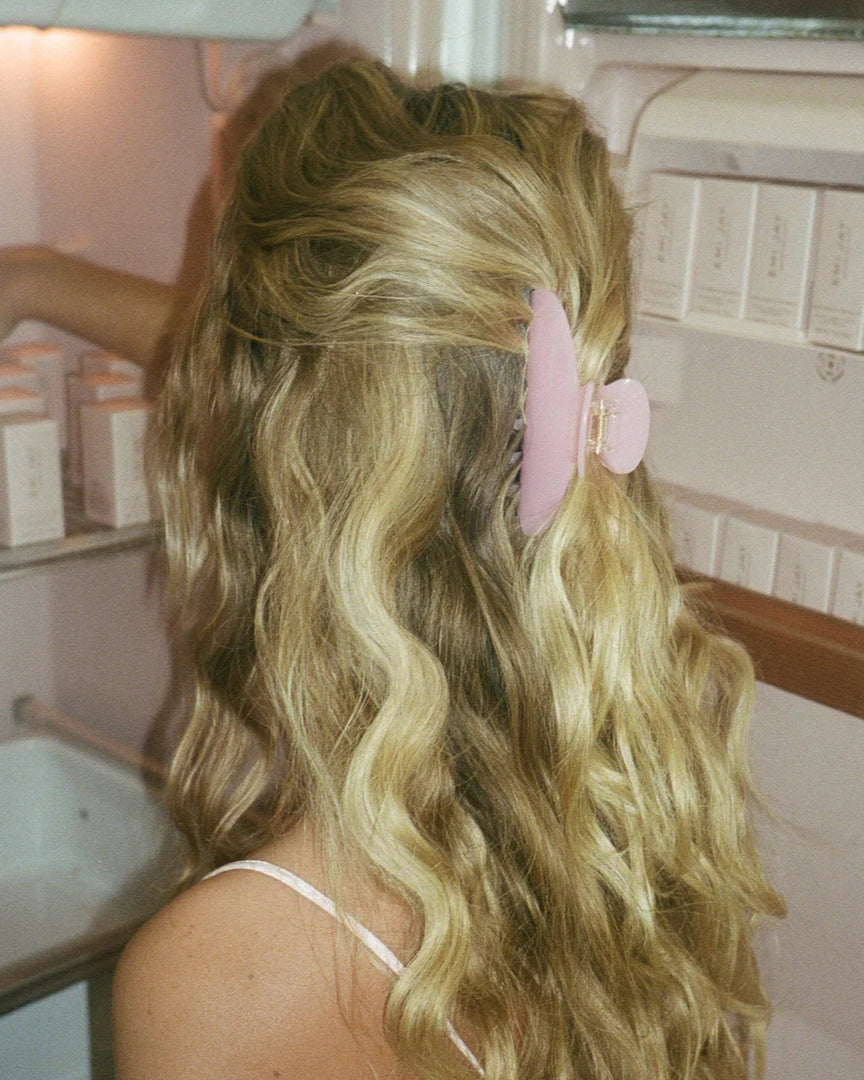 Person with wavy blonde hair and a pink hair clip in a bathroom setting