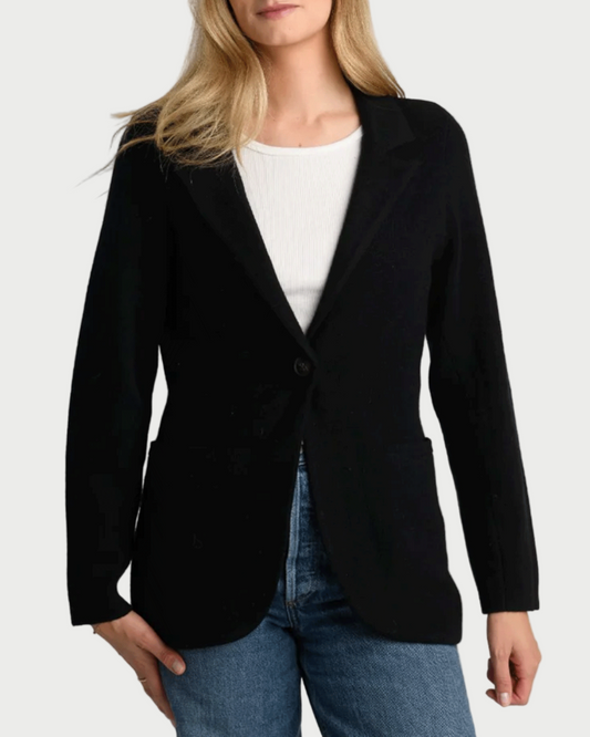 Woman wearing a black blazer over a white top and blue jeans on a gray background