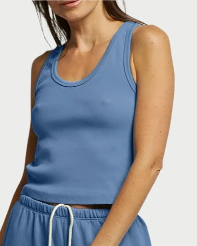 A woman stands against a neutral background wearing the Blondie - Carolina Blue from perfectwhitetee, a light blue sleeveless top and matching jogger pants with a white drawstring, made from a luxurious cotton blend. Her brown hair is loosely tied back, and she has a relaxed yet confident expression.