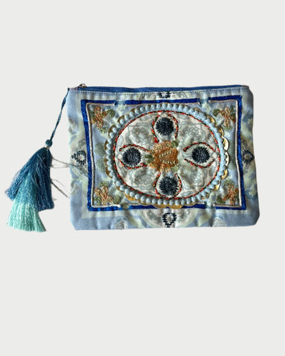 The DEBBIE KATZ Boho Pouch features intricate embroidery with a central floral design, complemented by blue and gold threads. It has a turquoise tassel on the zipper, making it an ideal decorative accessory for your beach bag.