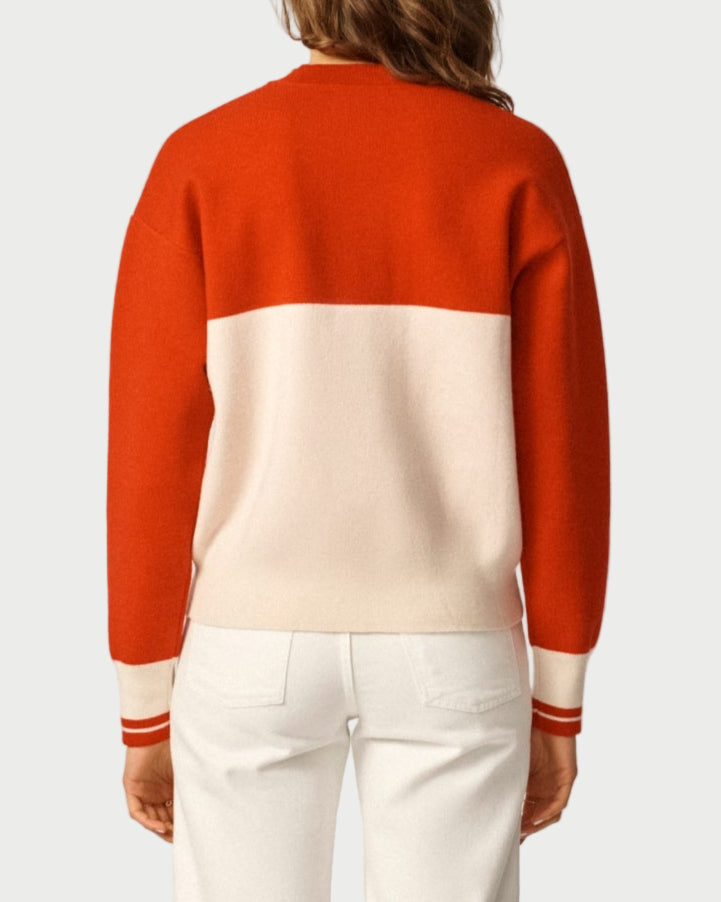 Person wearing a red and beige sweater with white pants on a plain background
