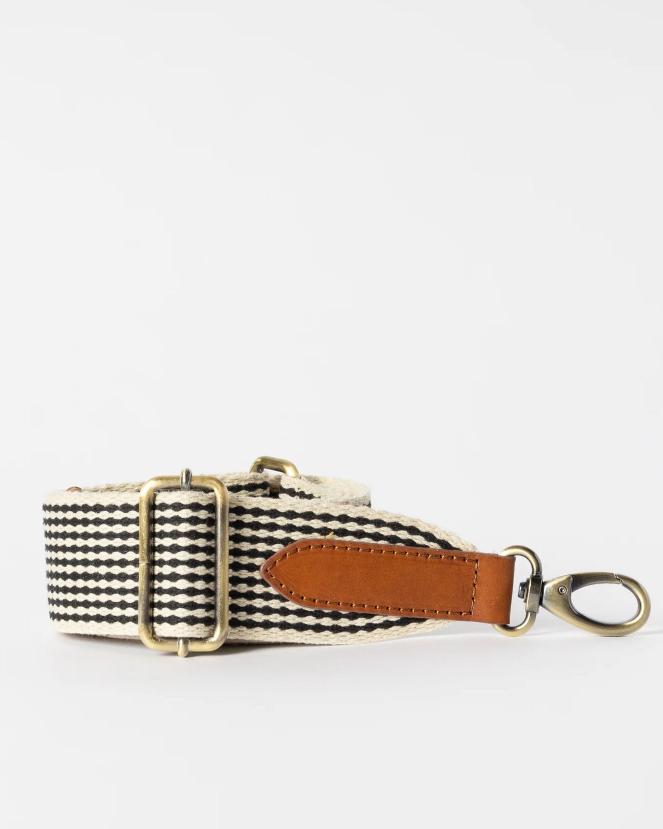 The O MY BAG Checkered Webbing Bag Strap features black and white stripes, an adjustable organic cotton design, brass hardware, a brown leather accent, and a metal swivel clasp, shown on a white background.