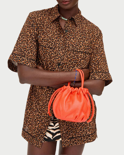 A model wearing a brown and black leopard print short-sleeve button-up shirt and holding a bright orange drawstring handbag against a plain white background.