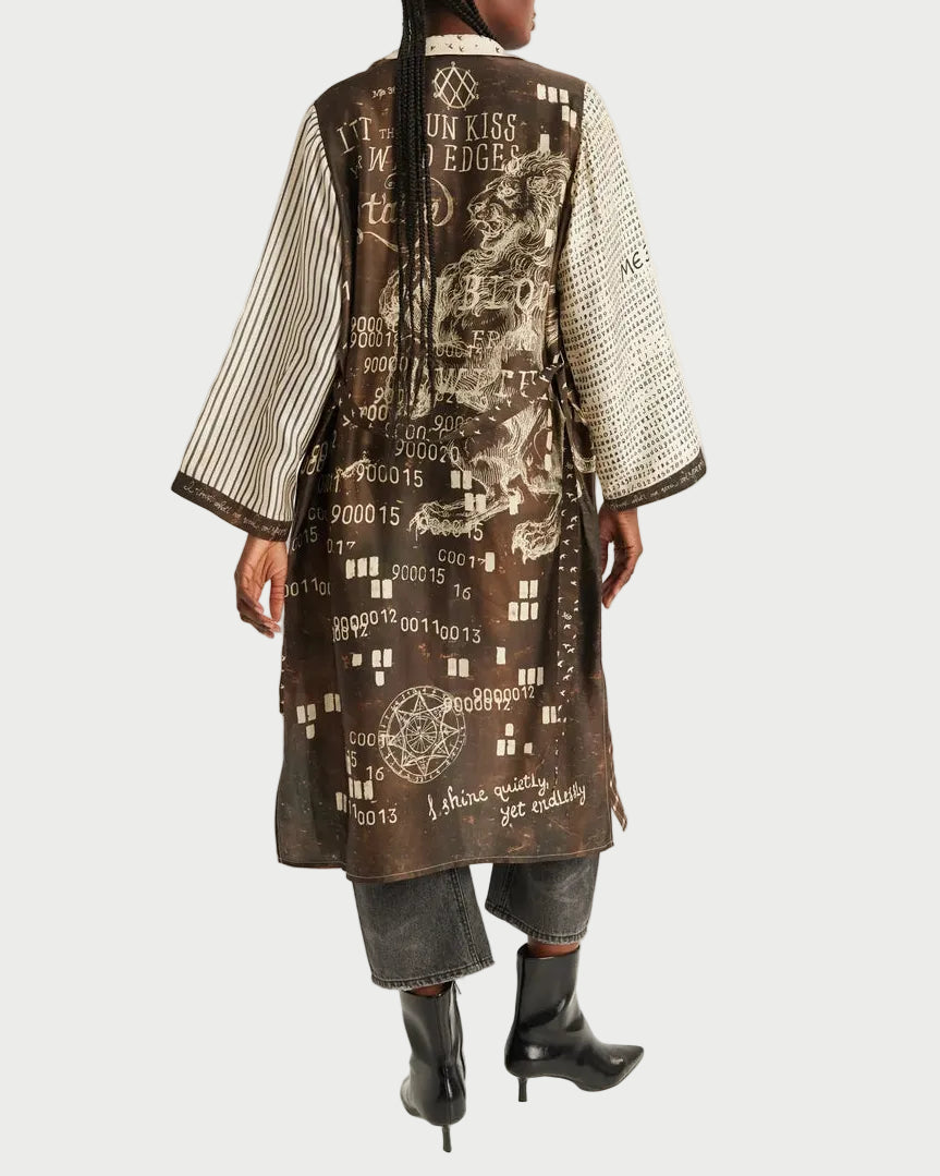 A model shown from the back wearing a long brown printed kimono-style coat with striped sleeves, dark cropped pants, and black ankle boots, photographed against a plain light gray studio background.