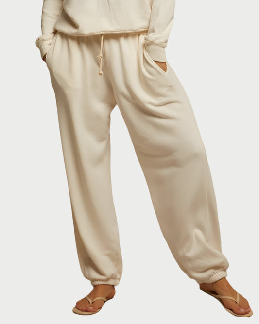 A person wears perfectwhitetee Drifter Beach Terry Sweatpants—loose-fitting, beige joggers with elastic waistband and cuffs. Only the lower half is visible, highlighting the oversized fit and sandals on their feet.
