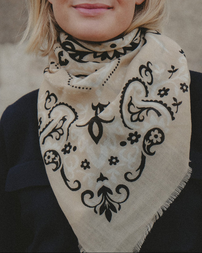Woman wearing a beige scarf with black patterns against a neutral background