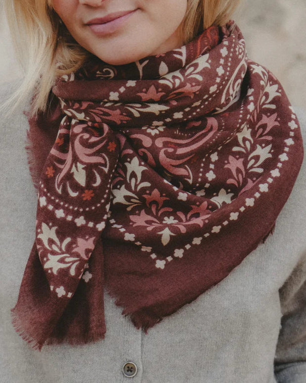A woman wearing a light gray button-up top and the Maison Lecomte Flament Saint Emilion Scarf, a maroon luxury square scarf with cream and pink floral patterns, wrapped around her neck.