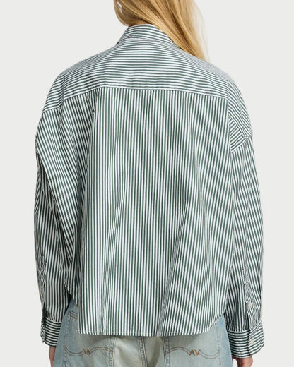 A person with long blonde hair, seen from the back against a white background, wears the Denimist Cropped Stripe Shirt by Denimist— a loose-fitting cotton button-down with black and white vertical stripes—paired with light blue jeans.