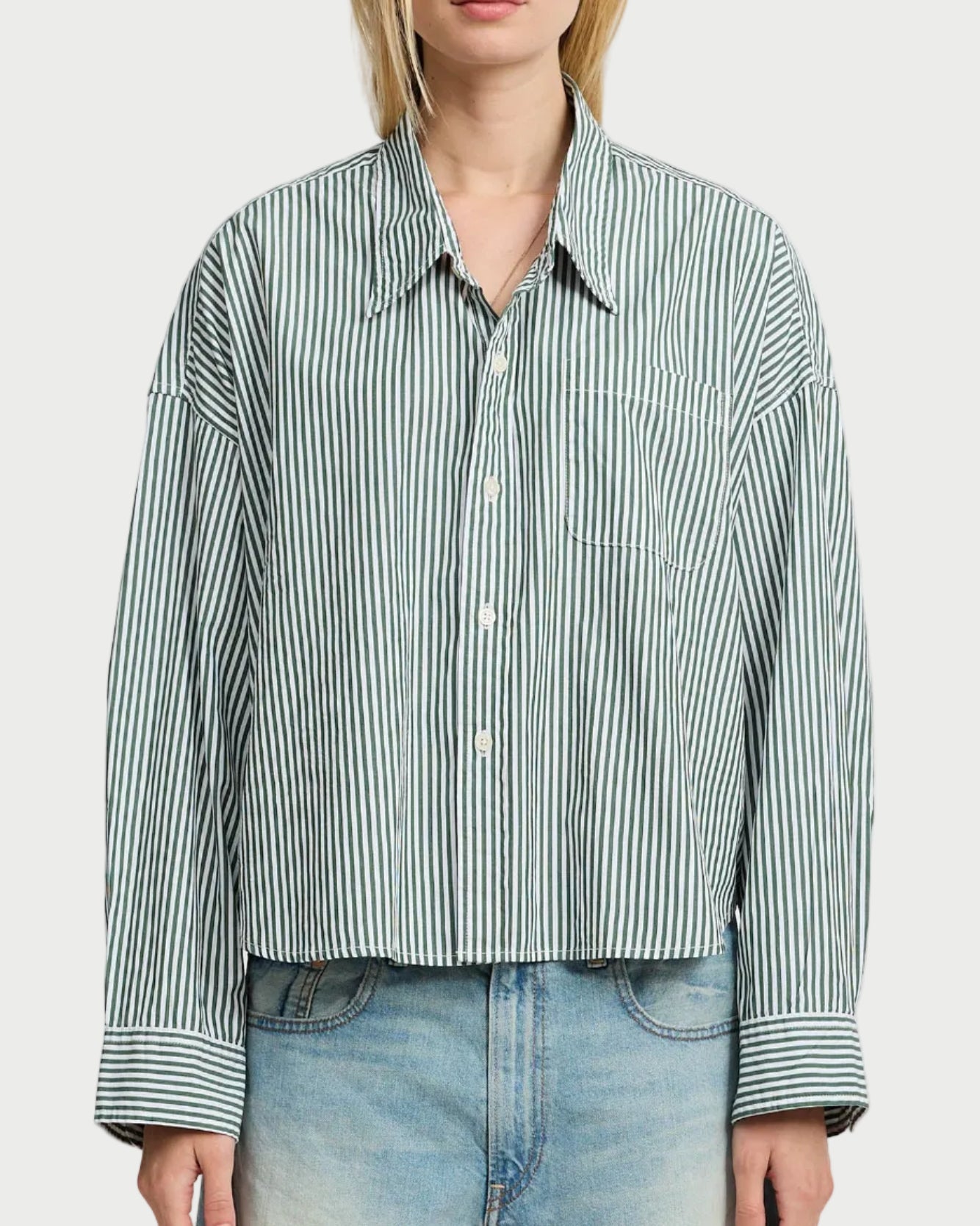 A person wears the Denimist Cropped Stripe Shirt—loose-fitting with white and green stripes, long sleeves, chest pocket—paired with light blue denim jeans. The shirt is by Denimist, and the person’s head is partially out of frame.