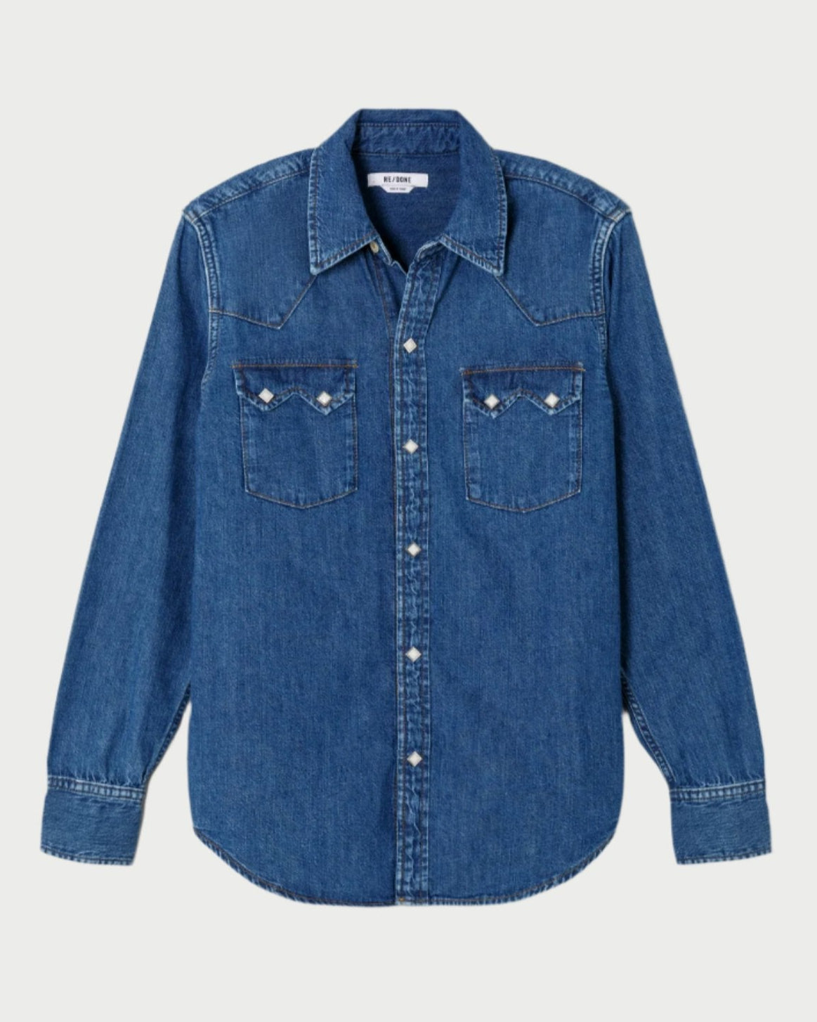 The 50s Western Shirt by RE/DONE showcases a long-sleeved design in deep denim blue, complete with a button-up front and two chest pockets featuring button closures. Its pointed collar and visible stitching on the shoulders, cuffs, and hem perfectly embody the denim-on-denim trend.