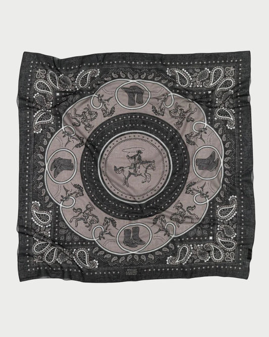 The Maison Lecomte Flament Rodeo Scarf features a black and gray bandana pattern with a central cowboy on horseback, horses, boots, hats, and paisley borders. Its relaxed look comes from the slightly wrinkled fabric.