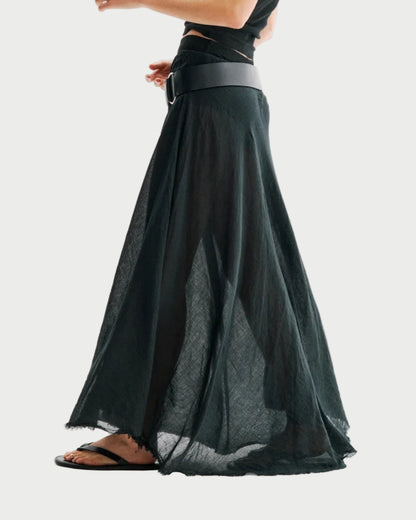 A person wearing the All III Elysia Maxi Skirt by All III—a black, sheer maxi skirt styled with a wide belt—paired with a black top and black sandals, shown from the side against a plain white background.