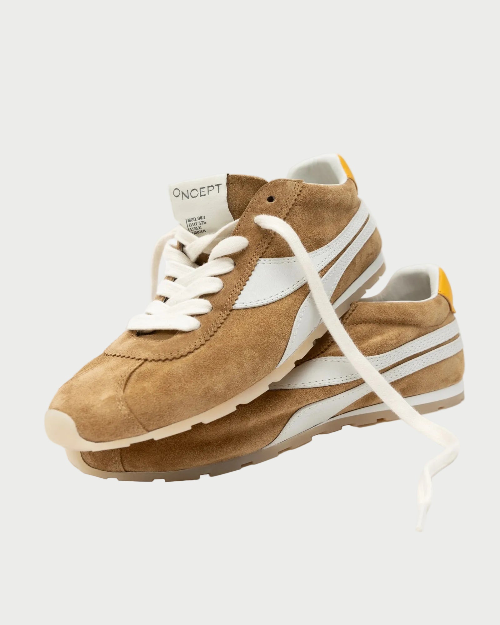The Oncept Essex Sneaker - Ginger by Oncept is a tan suede sneaker with white laces, white side stripes, and a yellow heel accent, sustainably crafted and shown on a light gray background.