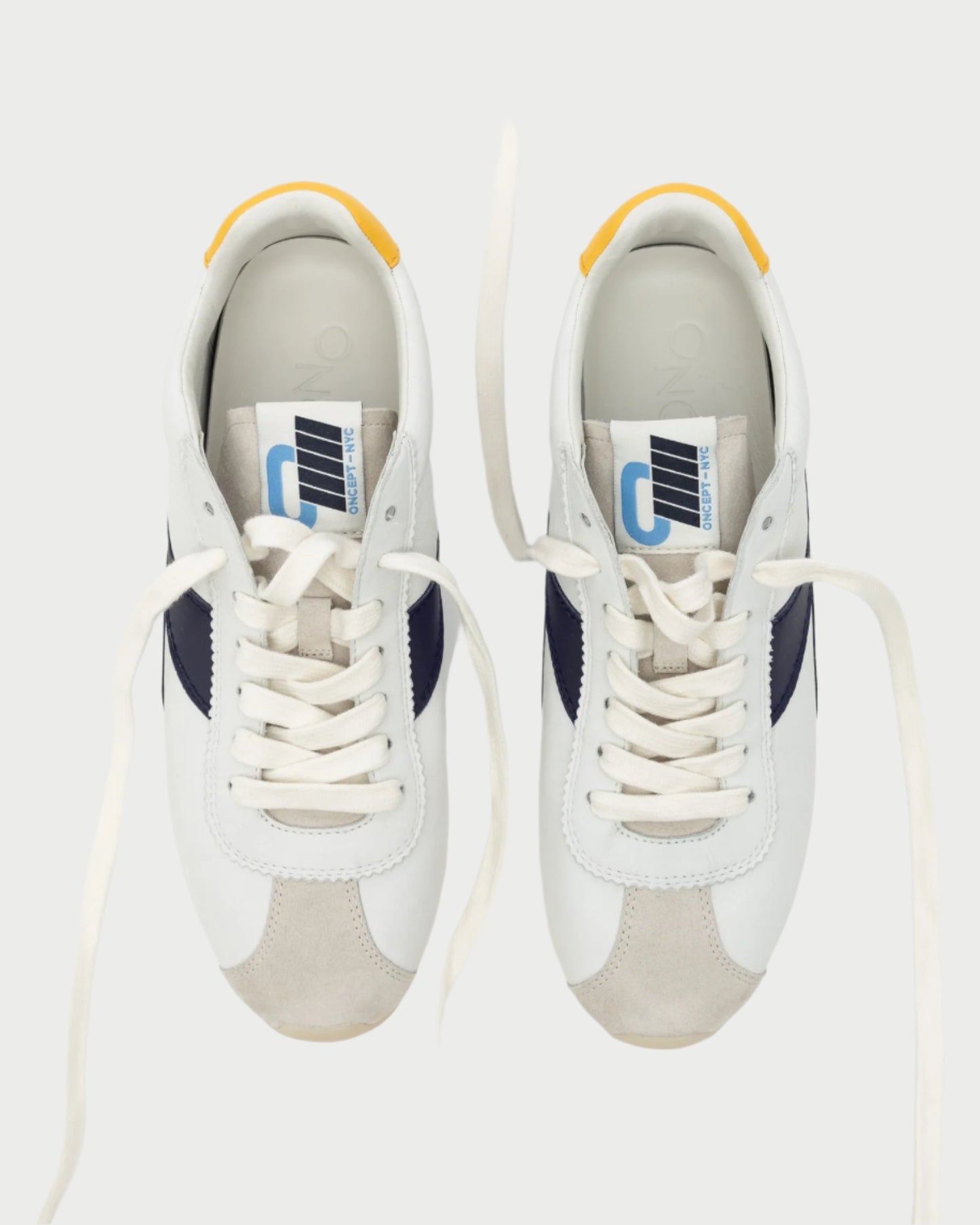 A top view of Oncept's Essex Sneaker shows sustainable design with black accents, white laces, yellow heel tabs, and blue and white tongue tags. The versatile footwear is set against a plain background.