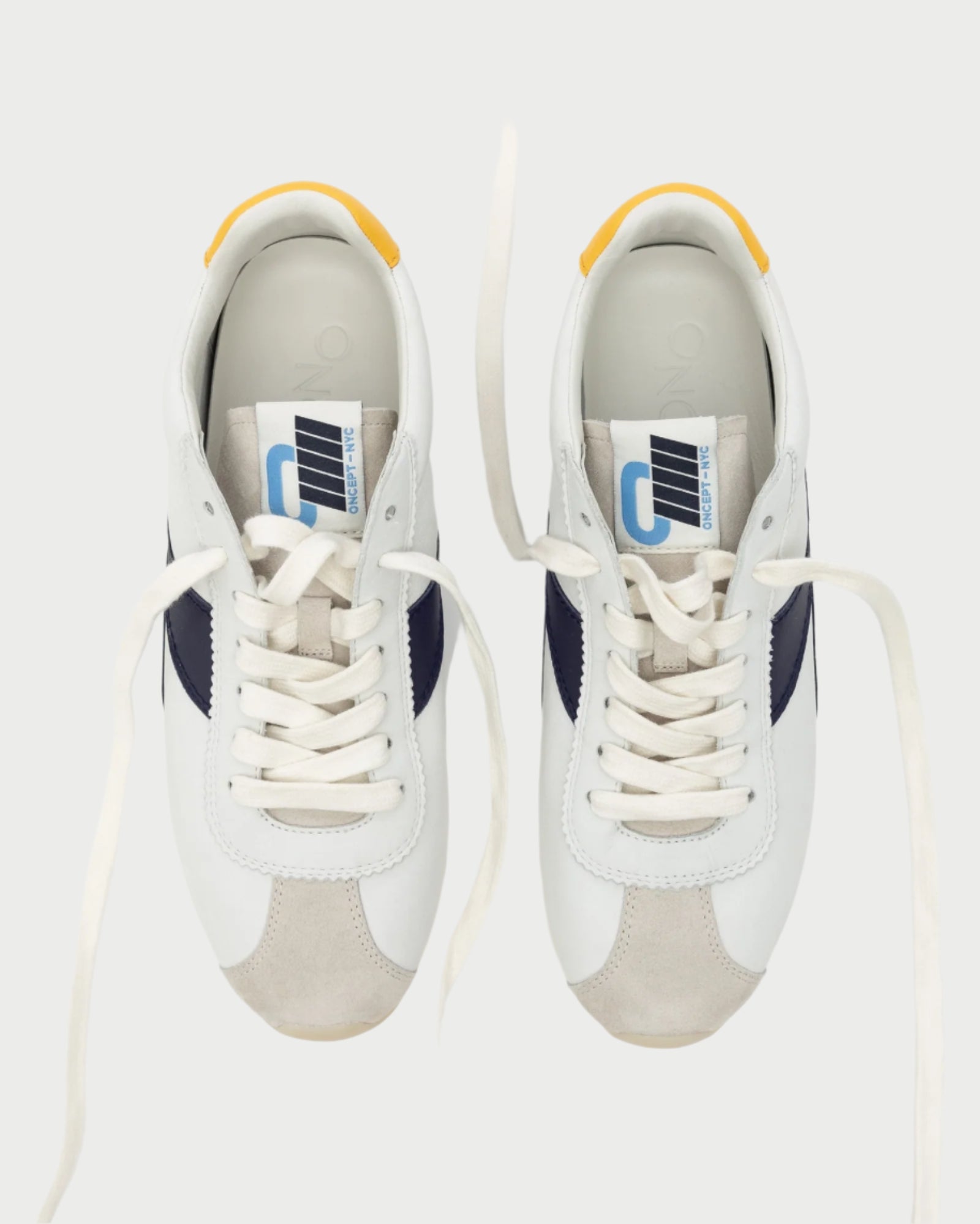 A top view of Oncept's Essex Sneaker shows sustainable design with black accents, white laces, yellow heel tabs, and blue and white tongue tags. The versatile footwear is set against a plain background.