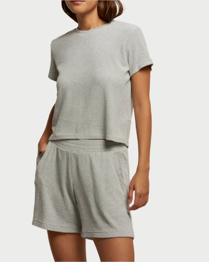 A person in a light gray, perfectwhitetee loungewear set called the Eve Loop Terry Tee, featuring a boxy-fit short-sleeve top and matching shorts. The casual outfit looks soft and offers ultimate comfort against a plain white background.