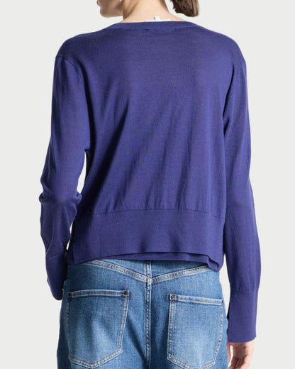 A person shown from the back wearing a cropped long-sleeve knit sweater in a medium periwinkle blue-purple color, paired with blue jeans, against a plain light gray studio background.