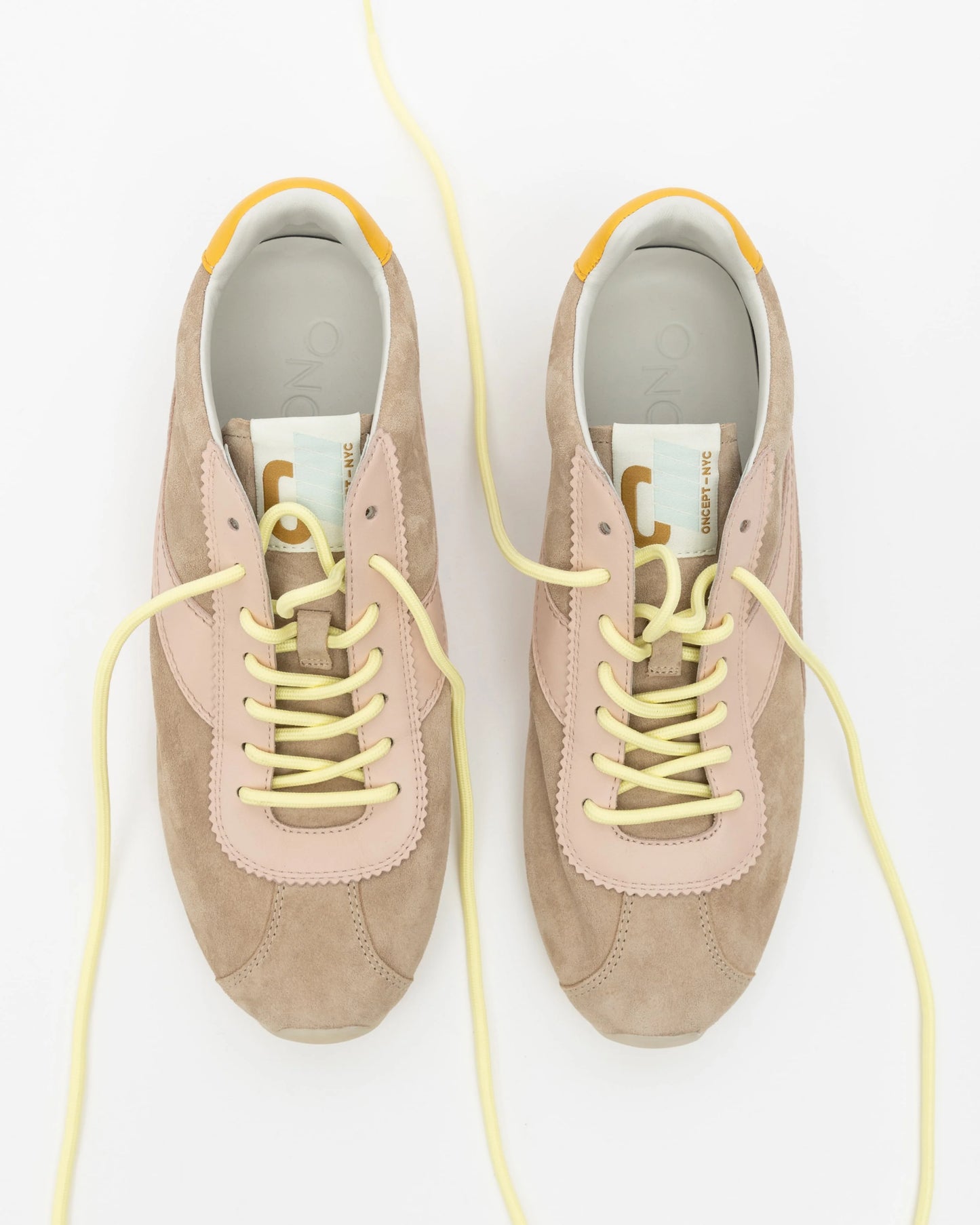 Pair of beige sneakers with yellow laces on a white background