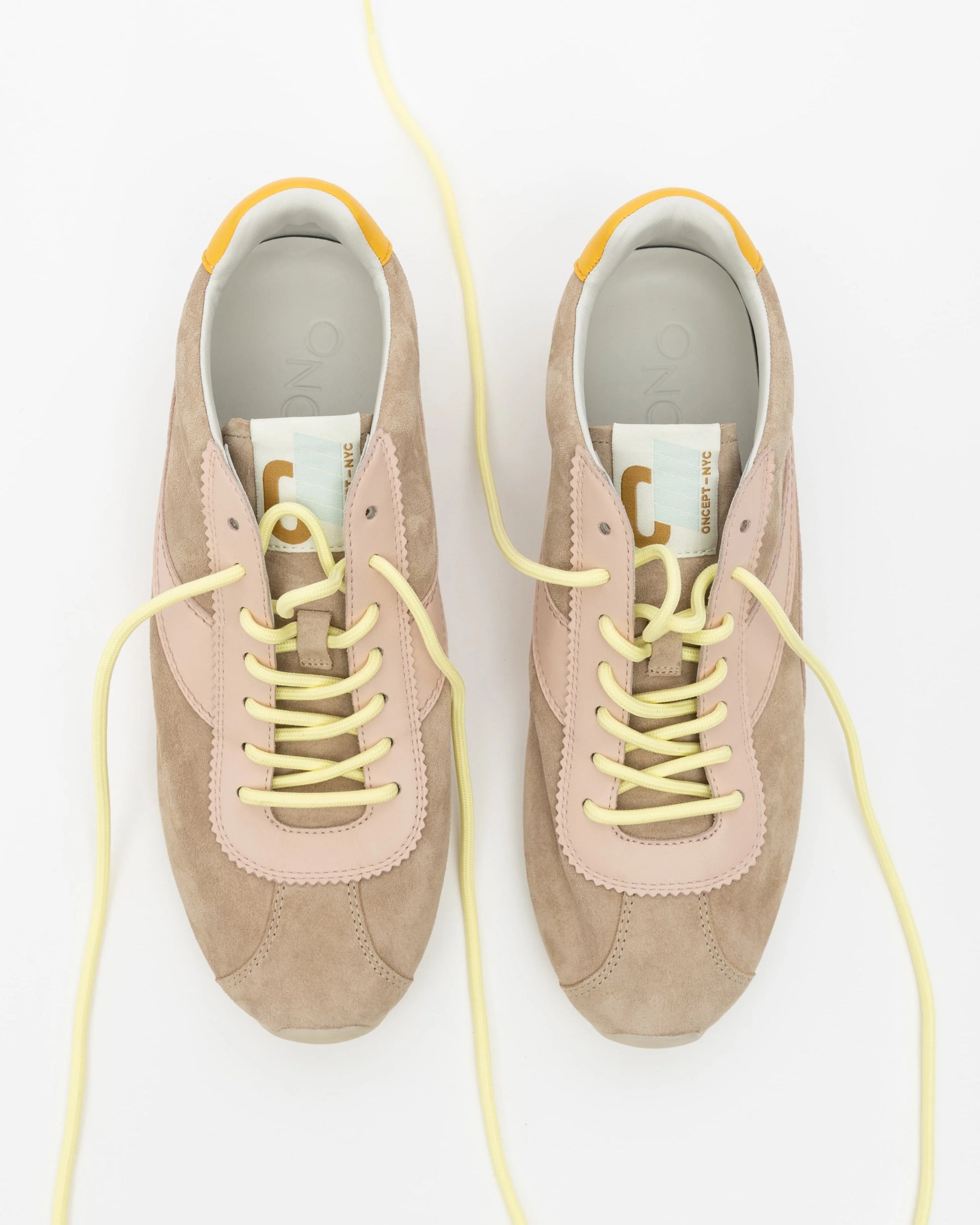 Pair of beige sneakers with yellow laces on a white background