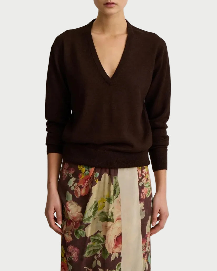 A person wears the Smythe Boyfriend V-Neck Sweater in dark brown, paired with a floral skirt featuring pink, yellow, and green hues on a light background.