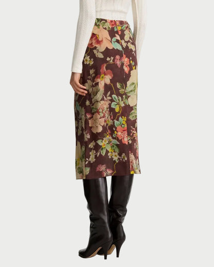 A person wearing a white sweater, the Smythe Asymmetrical Overlay Skirt by Smythe in a brown floral print, and tall black heeled boots, shown from the back against a plain background.