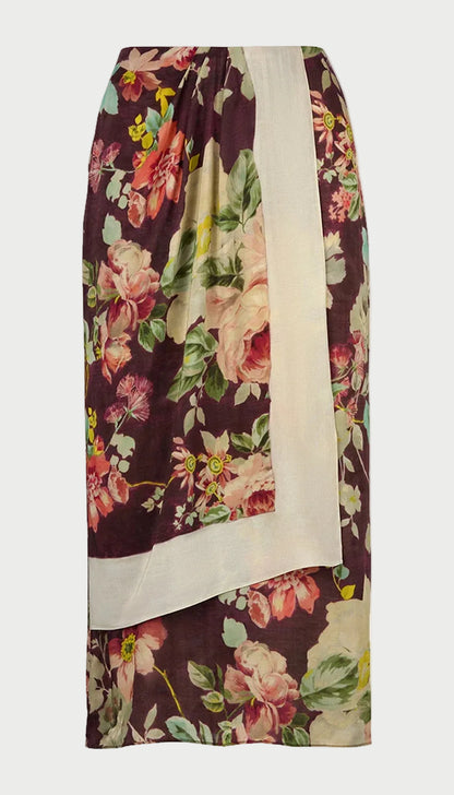 The Smythe Asymmetrical Overlay Skirt by Smythe features a burgundy background adorned with large floral prints in pink, yellow, and green. This midi skirt is designed with a wide off-white border along one side, creating an asymmetrical, draped effect that resembles an overlay—perfect for making a statement.