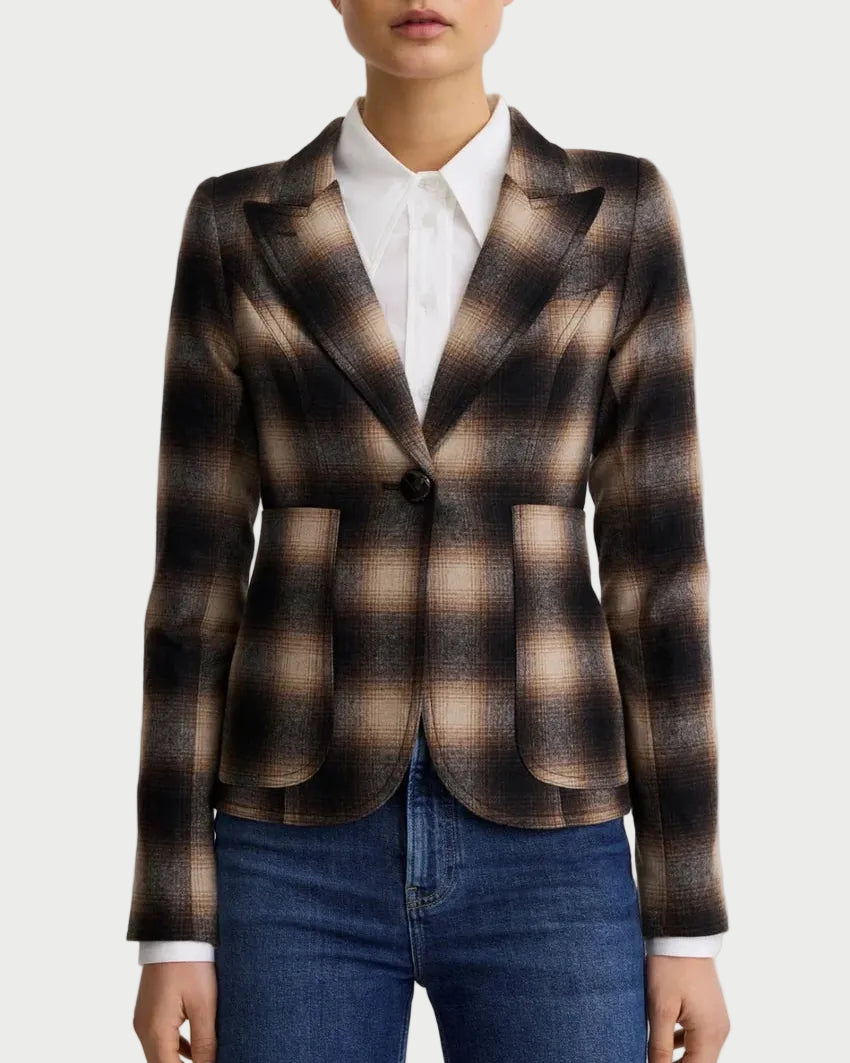 A woman modeling a brown and beige plaid blazer over a white collared shirt and blue jeans, photographed against a light gray studio background.