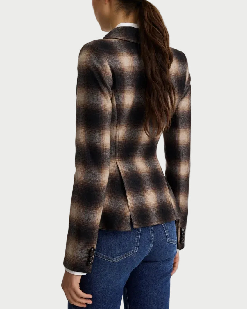 A woman shown from the back wearing a brown and beige plaid blazer with dark blue jeans, set against a plain light gray studio background.