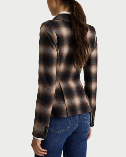 A woman shown from the back wearing a brown and beige plaid blazer with dark blue jeans, set against a plain light gray studio background.