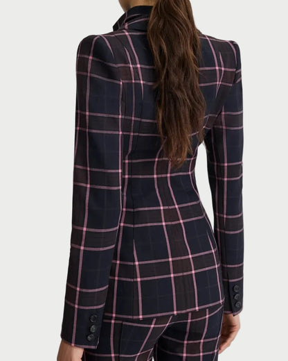 A woman shown from the back wearing a tailored navy blazer and matching trousers with a pink windowpane plaid pattern, against a light gray studio background.