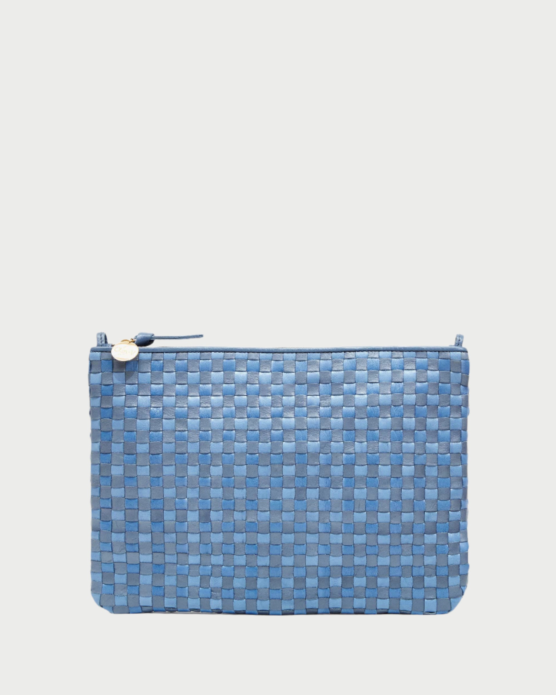 The CLARE V. Flat Clutch w/ Tabs is a versatile blue woven clutch featuring a basketweave texture on a white backdrop. Handwoven leather adds elegance, and it’s adorned with a small gold circular charm on the zipper.