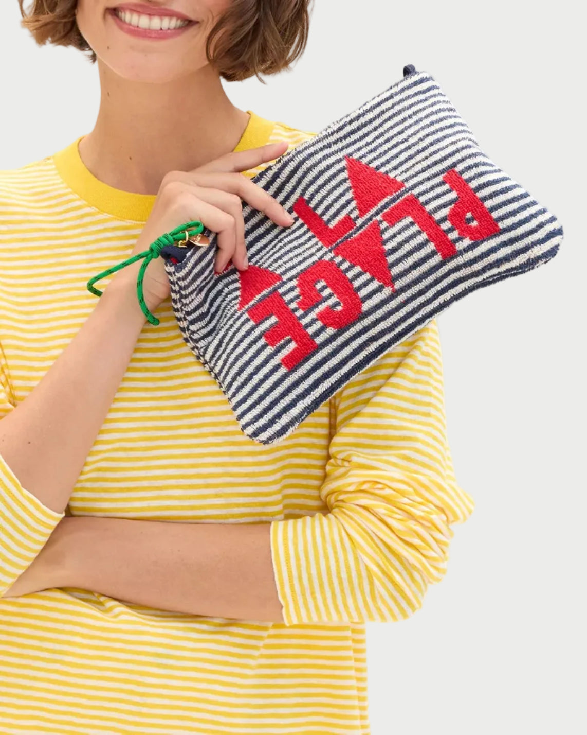 Woman holding a striped pouch with 'PLAGE' text, wearing a yellow striped shirt.