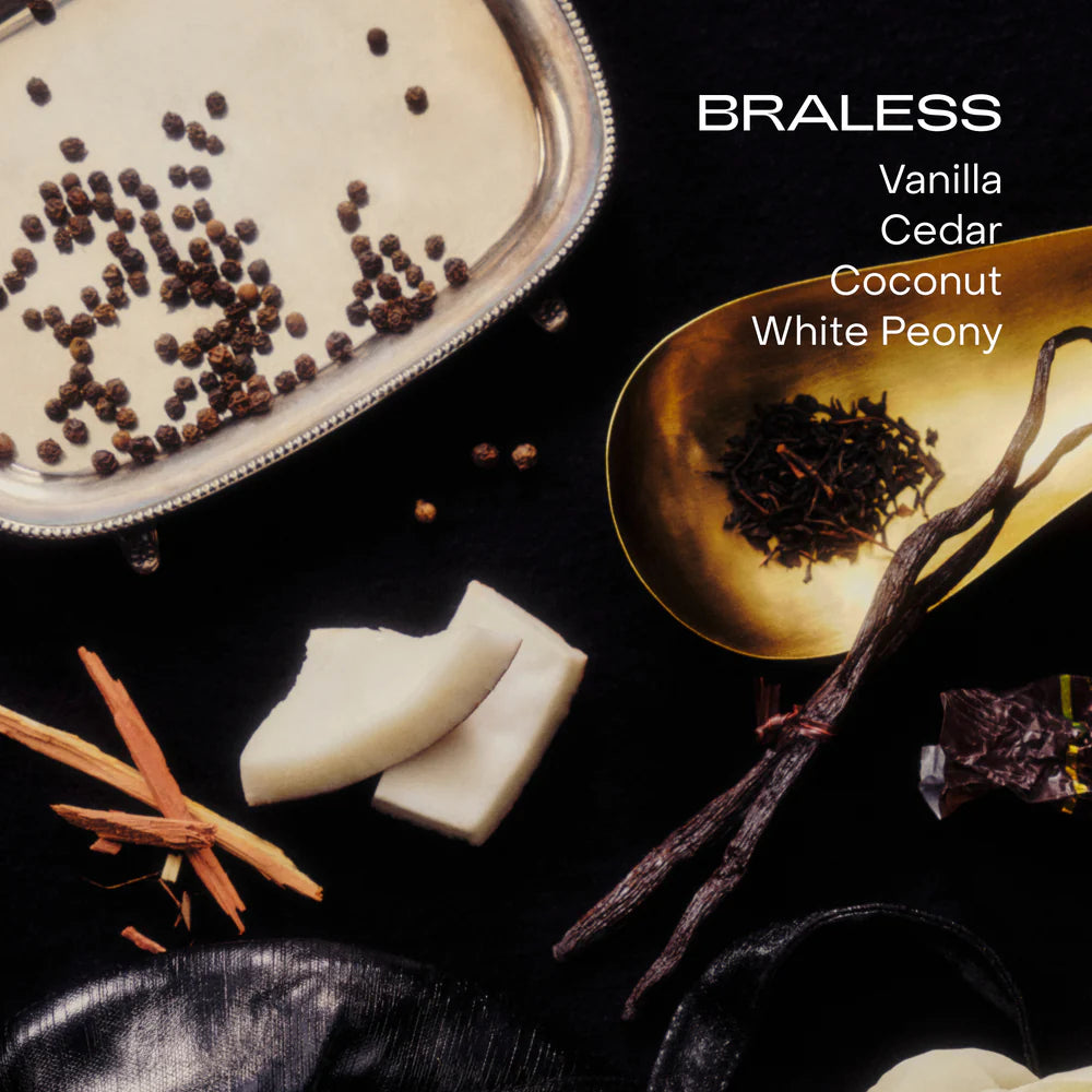 A flat lay of vanilla beans, cedarwood, coconut chunks, black peppercorns, and tea on black with the text: "BRALESS Vanilla Cedar Coconut White Peony" showcases the SIDIA Braless Candle, a non-toxic luxury home fragrance.