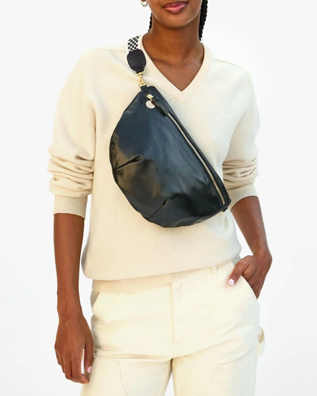 Person wearing a white sweater and pants with a black fanny pack on a white background