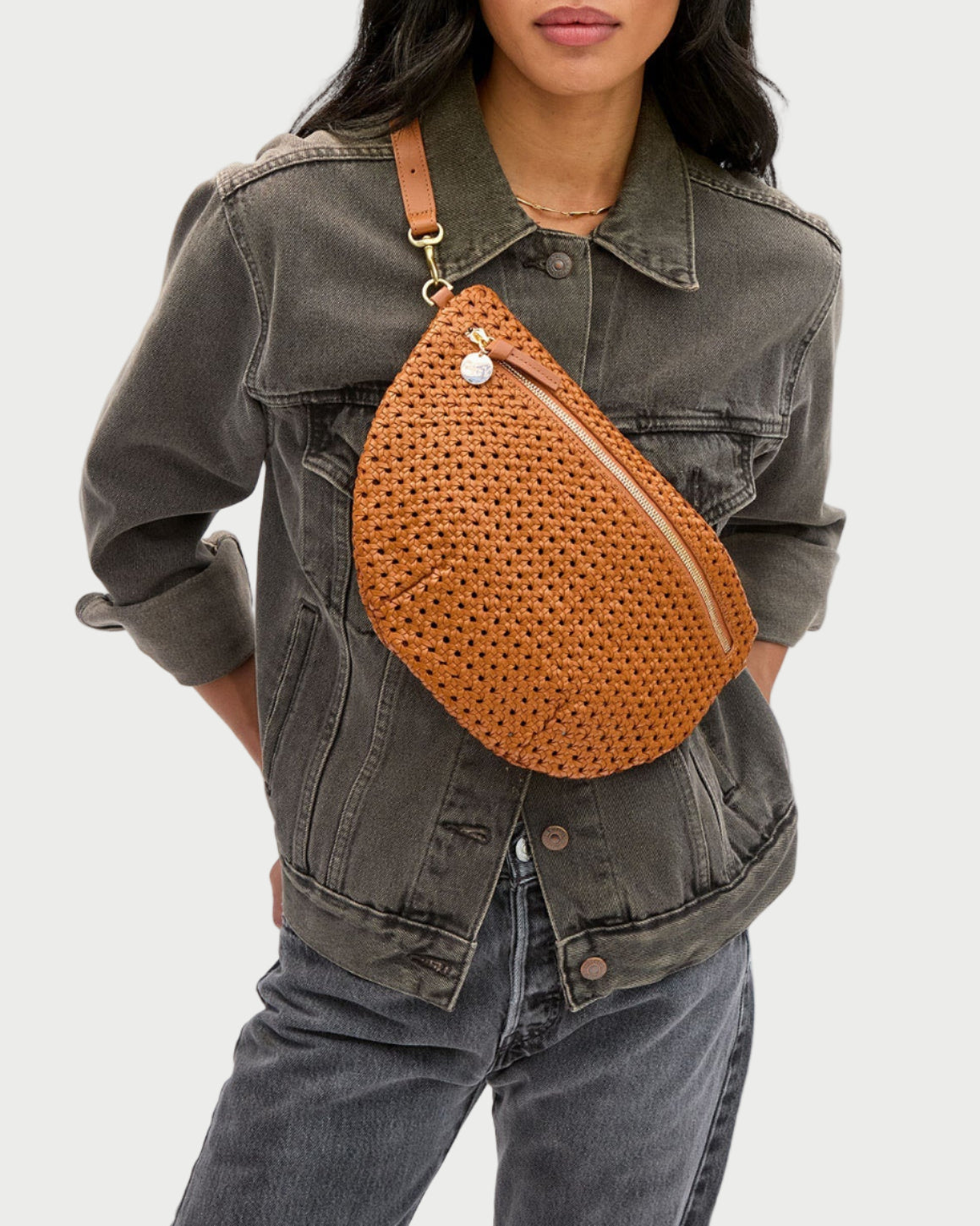 Woman wearing a brown woven crossbody bag with a plain background