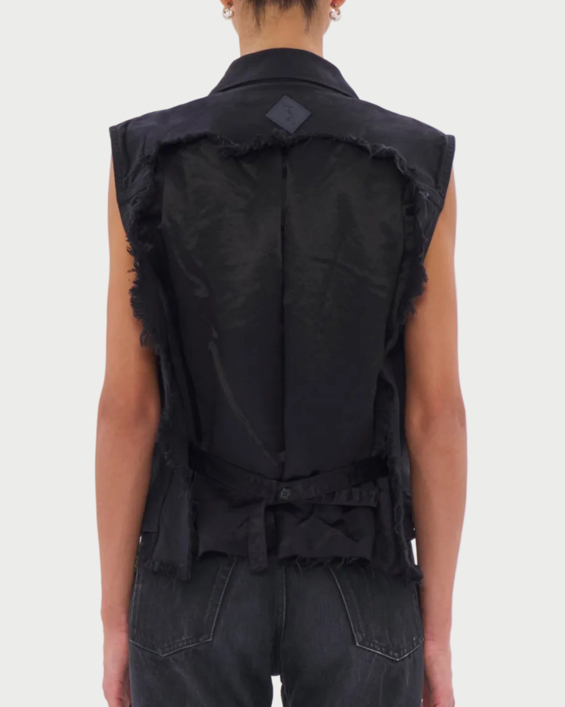 Person wearing a black sleeveless denim vest on a white background