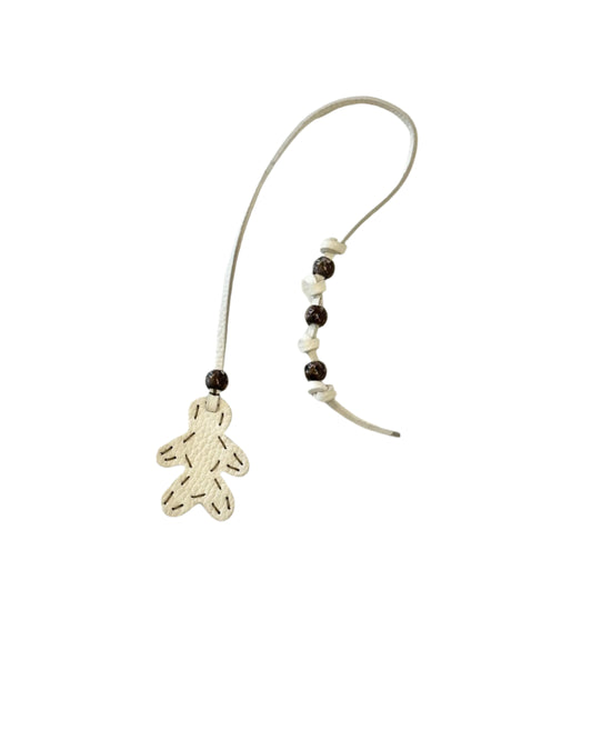 The Henry Beguelin Little Men Bag Charms feature a beige string with a stitched gingerbread-shaped ornament, alternating white and brown beads, and a handmade logo tag—crafted to highlight charming leather figures.